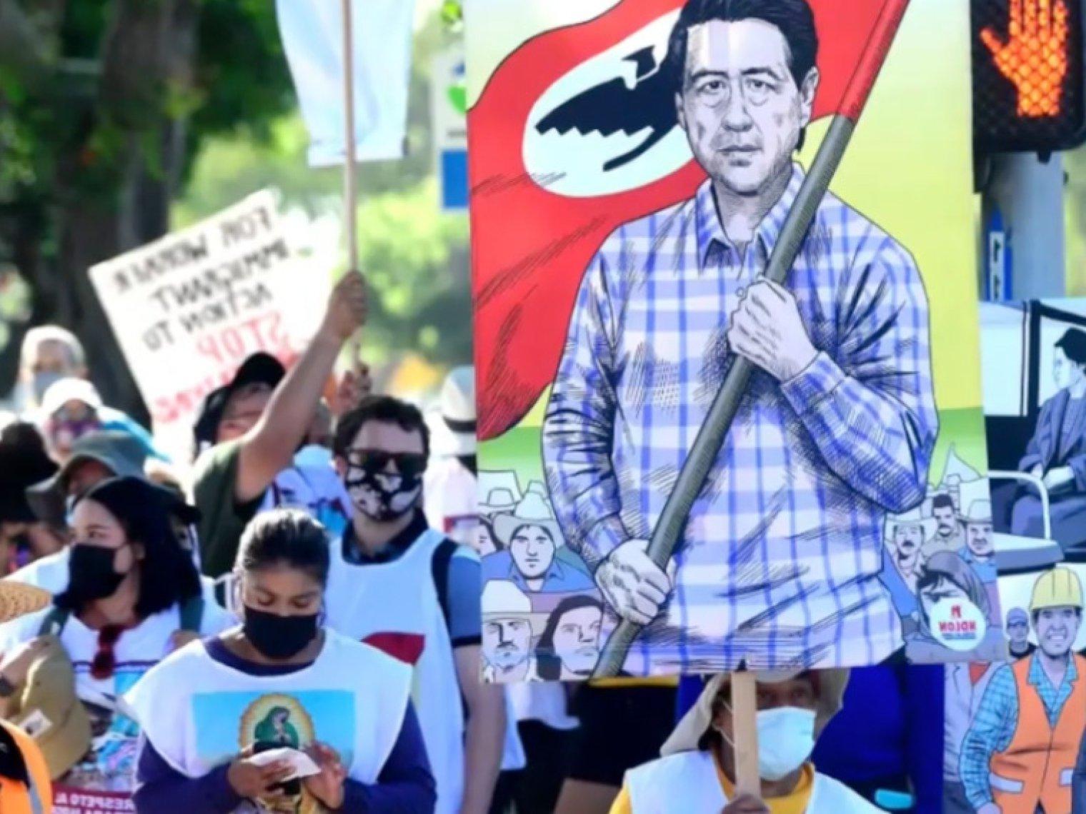 a group of protestors hold up signs and a cutout of cesar Chavez